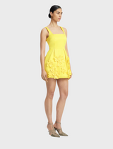  A model is dressed in a yellow floral dress, highlighting a playful and elegant fashion choice for warm weather.