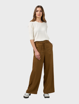 Bronze Polaris Pant draped over a chair, showcasing its modern style and rich color in a minimalist setting.