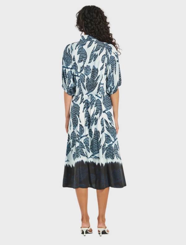 The model is dressed in a blue and white floral print dress, featuring a lively pattern that enhances her look.