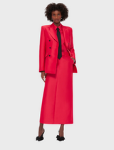 A woman wearing a red suit over a black shirt, standing confidently with a neutral expression.