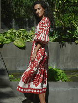 A woman wearing a red and white dress poses in front of a plain wall, her hands resting at her sides.