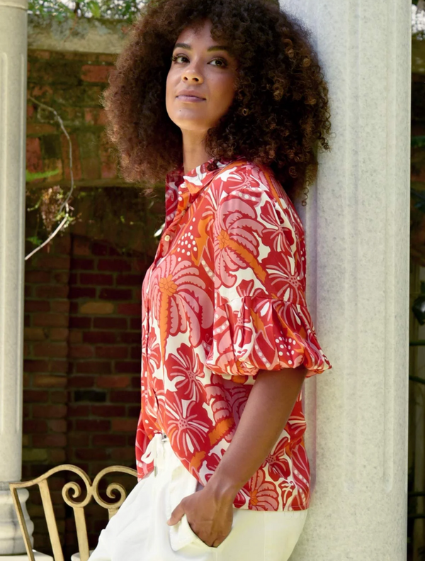  A woman with curly hair is dressed in a red and white shirt, looking cheerful.