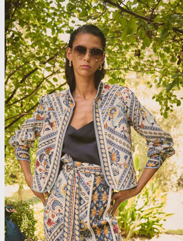 A woman in a blue jacket and pants relaxes on a bench, featuring the Aurora Reversible Viscose & Tencel Fringe Jacket.