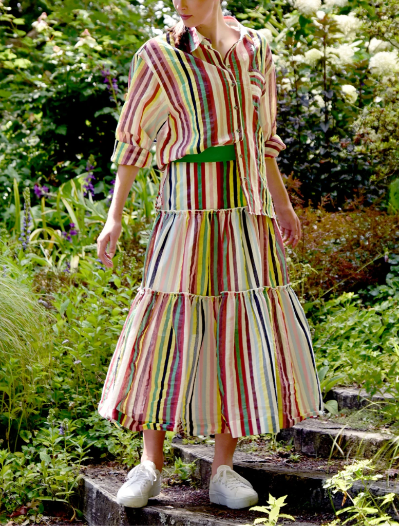 A woman in a striped dress strolls along a path surrounded by greenery.