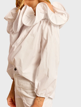 White Riva ruffled shirt displayed on a hanger, showcasing its elegant design and soft fabric texture.