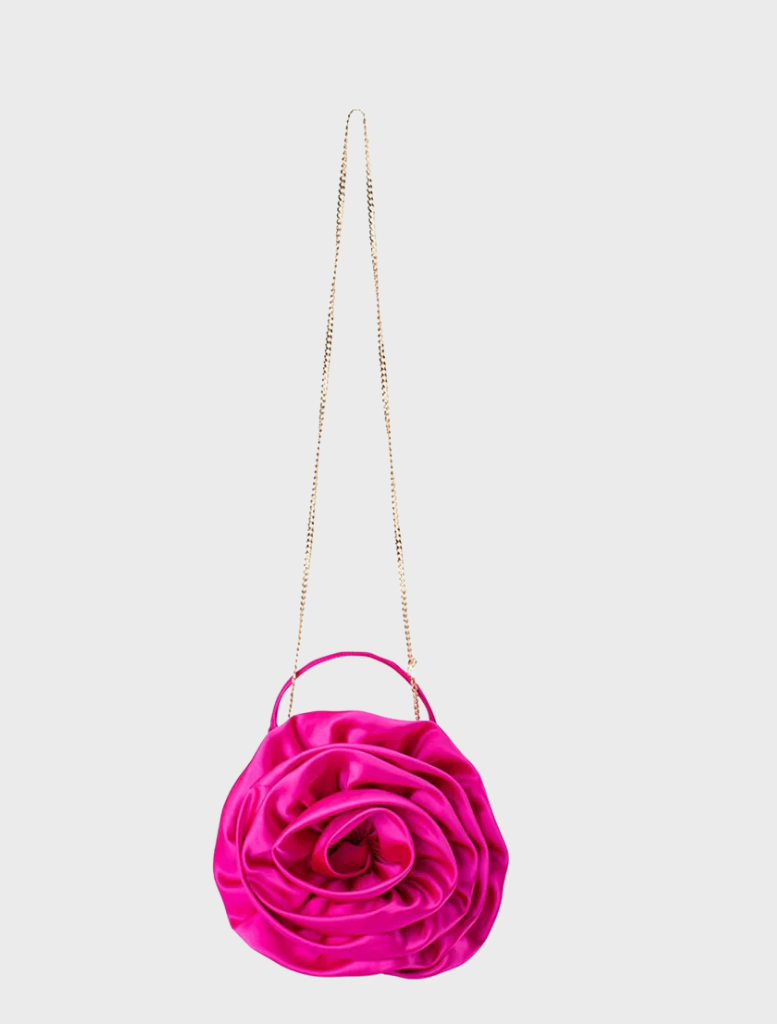 A pink satin flower bag, the Rosita Rosette Frame Bag in fuchsia, elegantly hanging from a delicate chain.