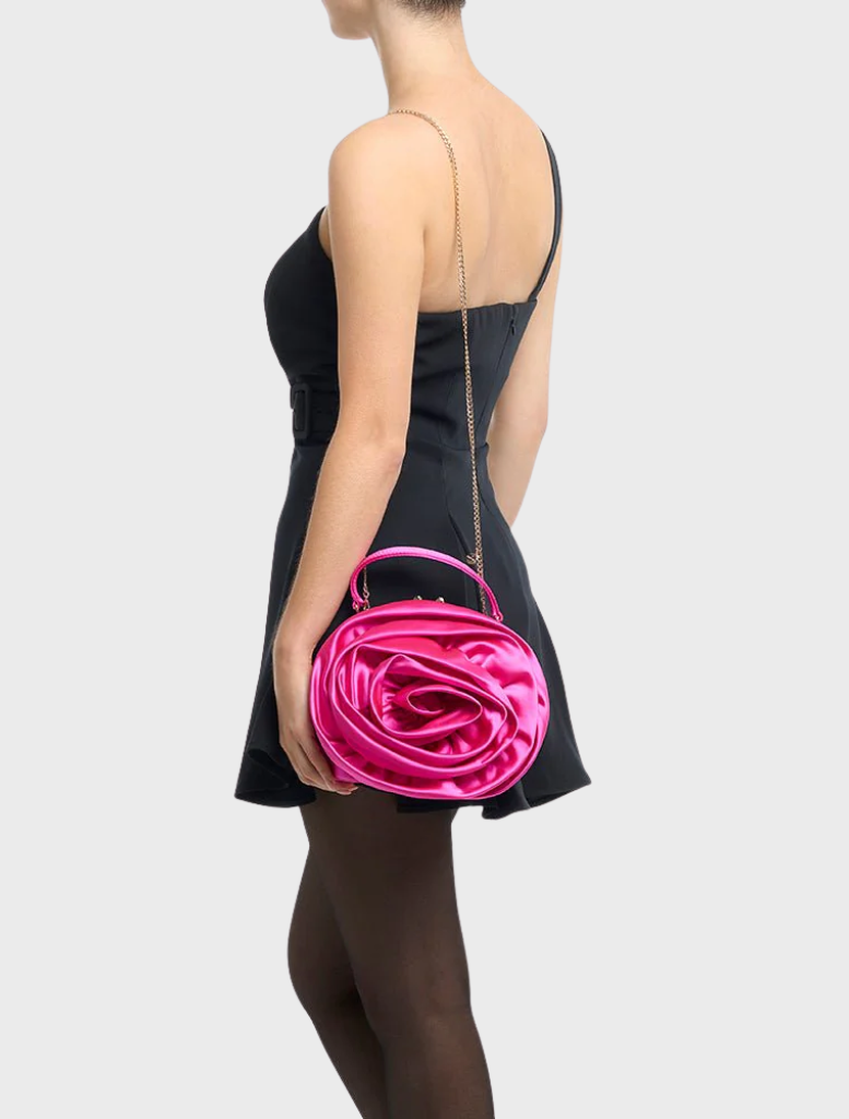 A woman in a black dress and tights holds a fuchsia Rosita Rosette Frame Bag, adding a pop of color to her outfit.