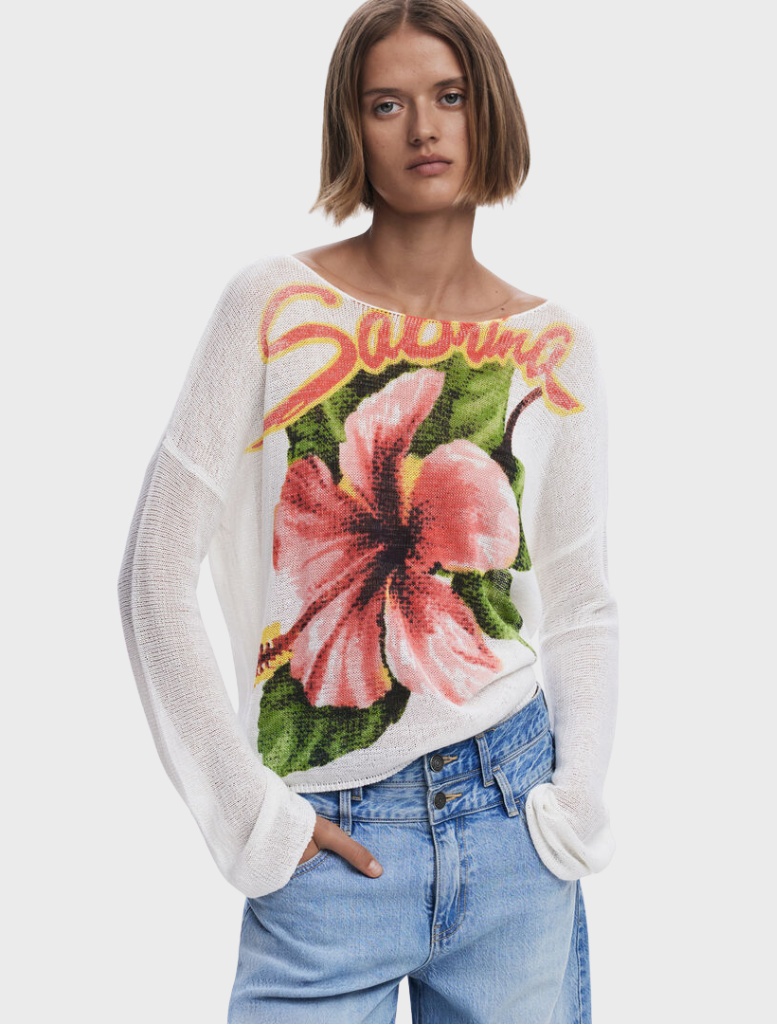 A model is seen in a white sweater that has a charming floral print.