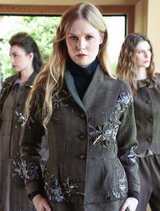 A gravel-colored Seam A Little Seam Jacket displayed on a hanger, showcasing its modern design and tailored fit.
