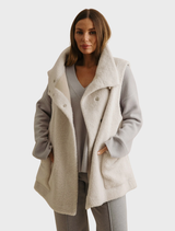 Latte-colored Sherpa cuddle gilet, designed for warmth with a soft texture and sleeveless style, perfect for layering.