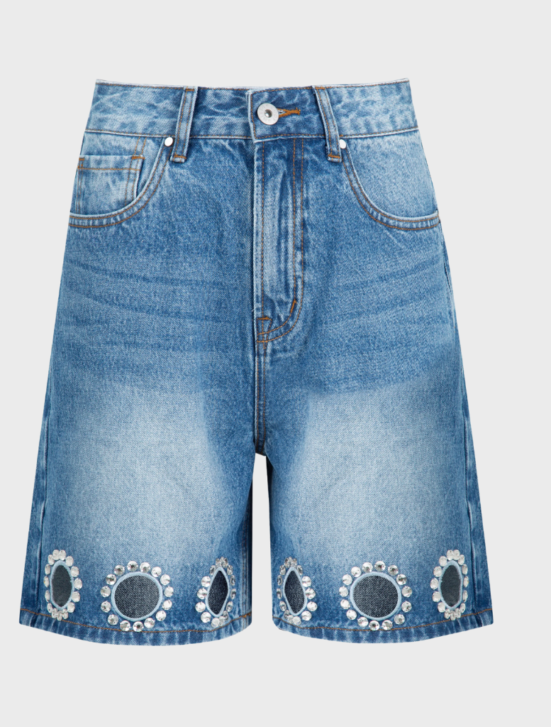 denim shorts stands casually, smiling at the camera.
