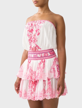 A feminine mini dress with a shirred waist and adjustable straps, showcasing a vibrant pink-and-white tile-inspired print.