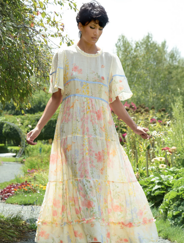 A woman in a vintage floral dress strolls through a vibrant garden, surrounded by blooming flowers and greenery.