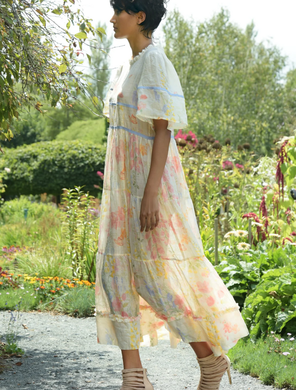  A woman wearing a floral dress walks gracefully through a lush garden filled with colorful flowers and plants.