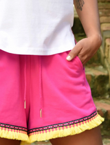 A woman in pink shorts and sneakers is posing on a balcony, exuding a cheerful and relaxed vibe.