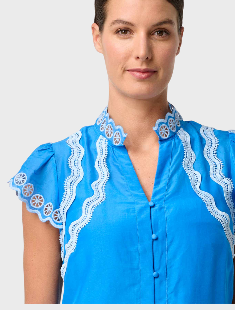A woman models a blue and white floral print dress, highlighting the Thalassa Embroidered Silk Cotton Flutter Sleeve Top.