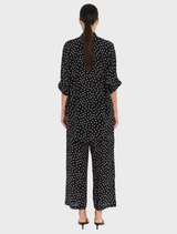 The model is dressed in a black polka dot overshirt and wide-legged pants, presenting a trendy and relaxed outfit.