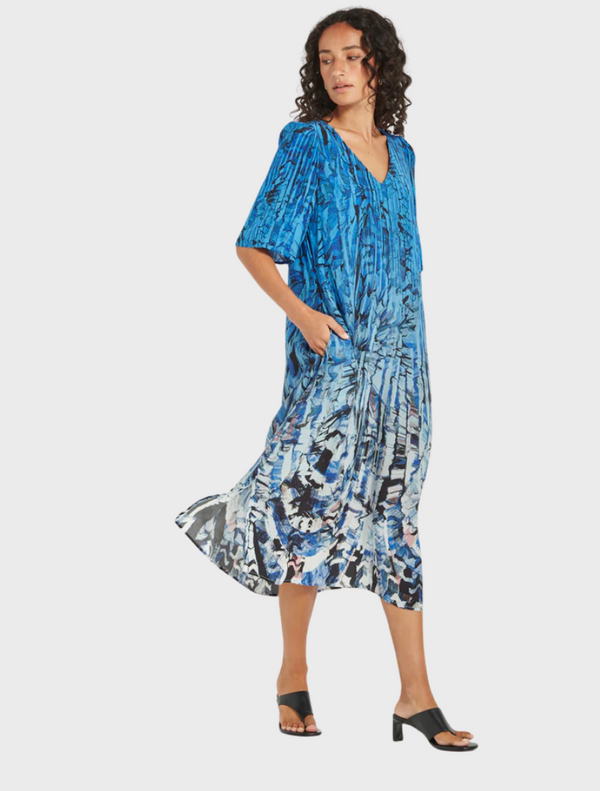 A woman in a blue and white floral print dress stands gracefully, showcasing the vibrant pattern of her attire.