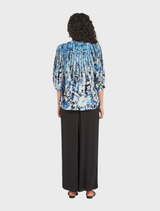 A model is dressed in a blue and black floral print top, featuring a blend of colors and a contemporary style.