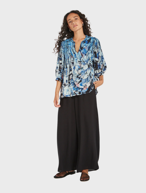 A model showcases a blue and black floral print top, highlighting its vibrant colors and stylish design.