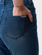 A woman wearing slim fit stretch jeans and a shirt stands, exemplifying a trendy and relaxed look.