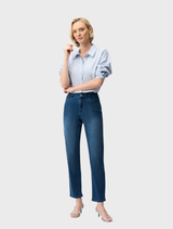 A woman in slim fit stretch jeans and a shirt stands confidently, showcasing a casual yet stylish outfit.