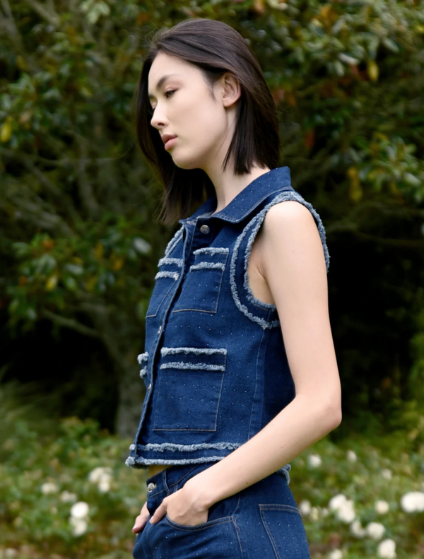 A woman dressed in a denim vest and jeans poses, highlighting her relaxed and fashionable look.