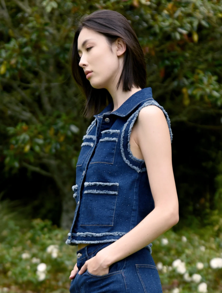 A woman dressed in a denim vest and jeans poses, highlighting her relaxed and fashionable look.