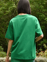 Back view of a woman wearing a green Sparkle Magic T-shirt, showcasing its vibrant color and casual style.