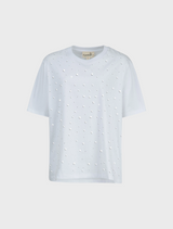 A woman dressed in a white Sparkle Magic T-shirt and a striped skirt smiles, embodying a chic and casual style.