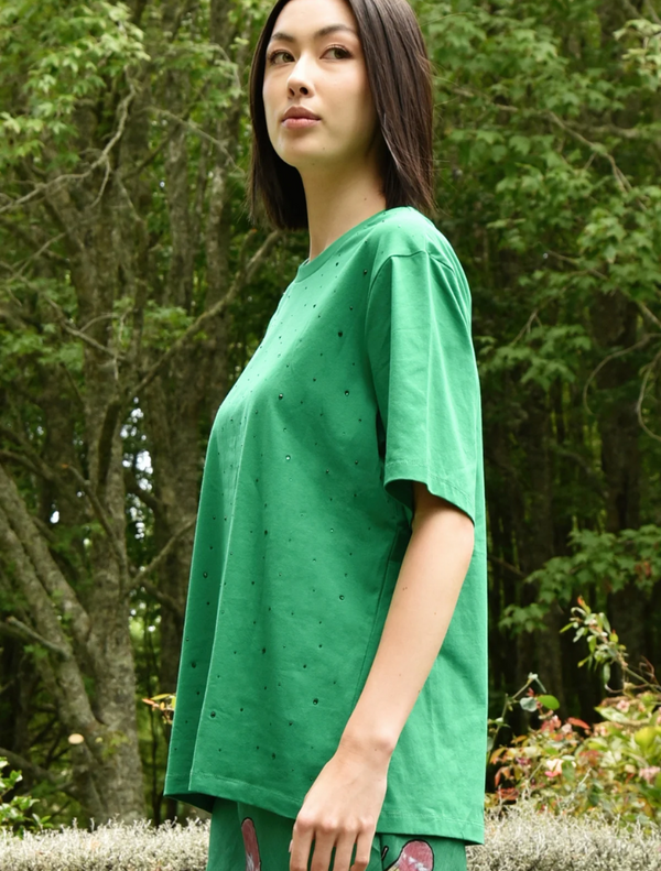 A woman wearing a green Sparkle Magic T-shirt poses for a photo, showcasing a cheerful expression and confident stance.
