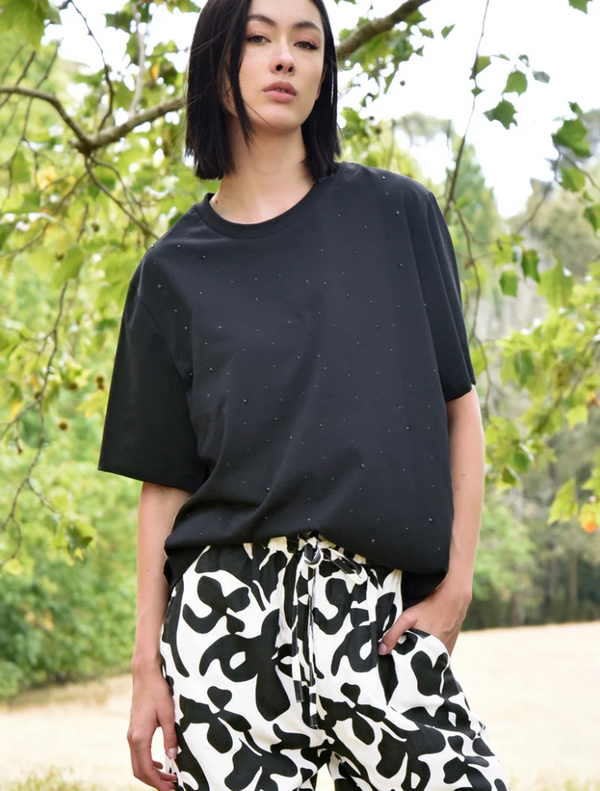 A woman wearing black and white pants with a black "Sparkle Magic" t-shirt.