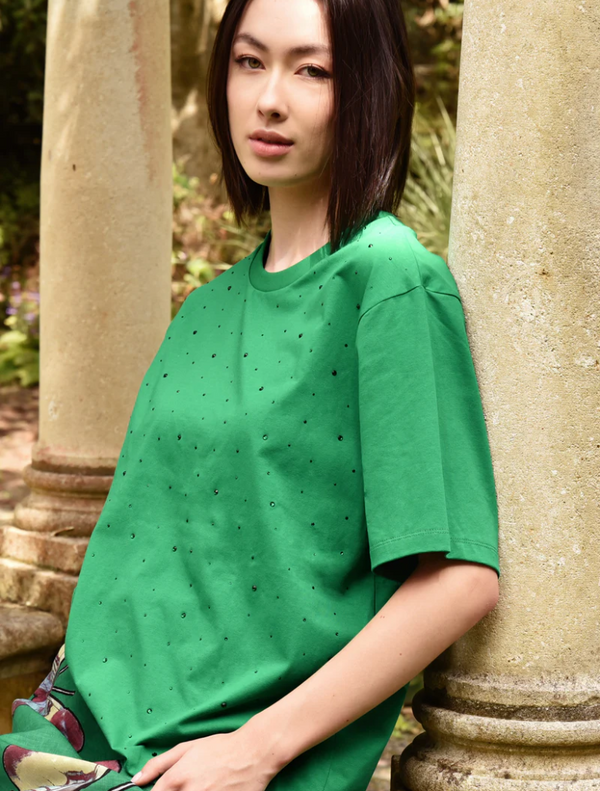A woman in a green Sparkle Magic T-shirt poses for a photo, smiling and looking directly at the camera.