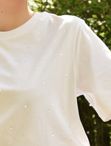 A woman in a white Sparkle Magic T-shirt paired with a striped skirt poses, highlighting her fashionable look.