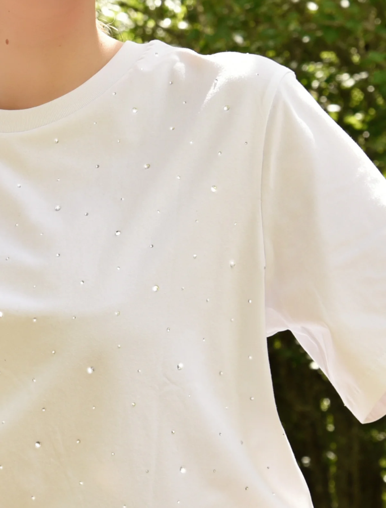 A woman in a white Sparkle Magic T-shirt paired with a striped skirt poses, highlighting her fashionable look.