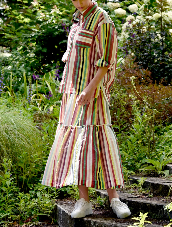 A woman wearing a striped dress walks down a scenic path lined with trees.
