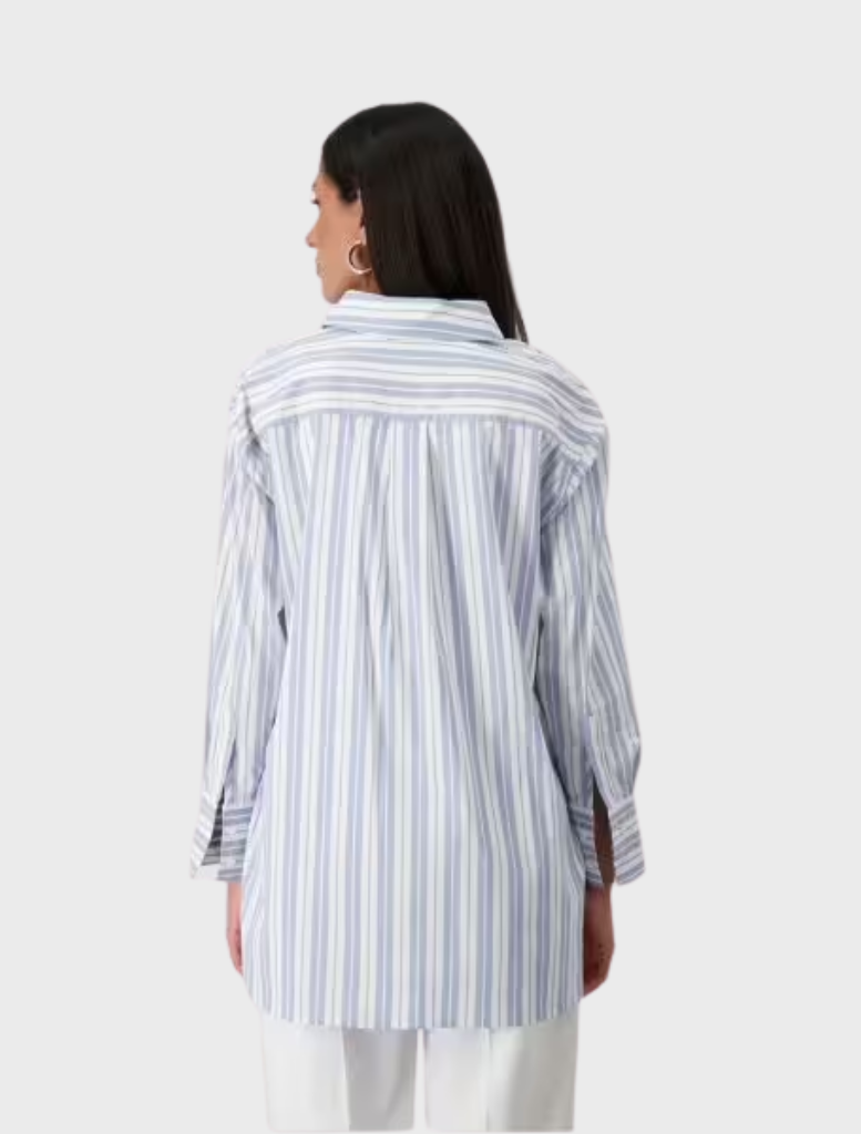 Back view of a woman in a blue and white striped shirt with a collar, set against a light sky background.