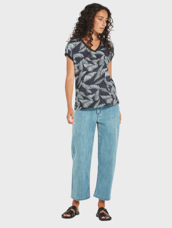 A model showcases a blue top adorned with a vibrant leaf print, highlighting a stylish and nature-inspired design.