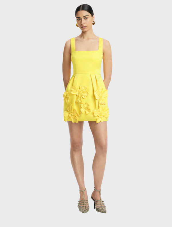 The model showcases a bright yellow dress featuring a floral pattern, exuding a lively and summery vibe.