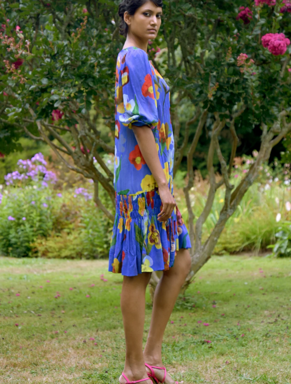A woman wearing a colorful cobalt floral tunic stands next to a tree, blending fashion with nature.