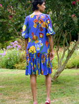 A woman in a cobalt floral dress walks through lush green grass, showcasing the Sweet Nothing Tunic design.