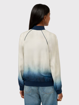 Ombre bomber jacket transitioning from white to blue, with floral accents and blue ribbing, designed for reversible styling.