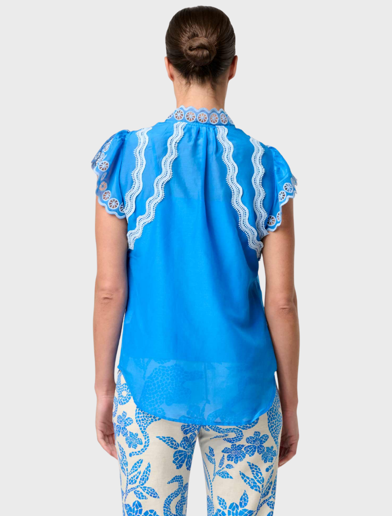 Back view of a woman in blue and white floral pants, wearing a blue topaz embroidered silk cotton flutter sleeve top.