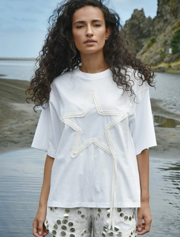 A woman wearing a white t-shirt with a star graphic, looking confidently at the camera.