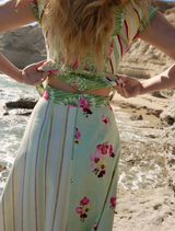 A woman stands on a rocky beach in a floral dress, displaying the Tillla Denim Maxi Skirt in Meadow Multi.
