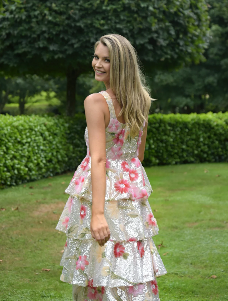A woman dressed in floral attire stands in front of a colorful garden, highlighting the beauty of nature around her.