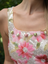 A woman in a floral dress stands amidst a beautiful garden, showcasing a variety of blooming plants and flowers.