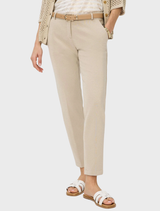 A woman in beige trousers and a white shirt stands confidently, showcasing a casual yet stylish outfit.