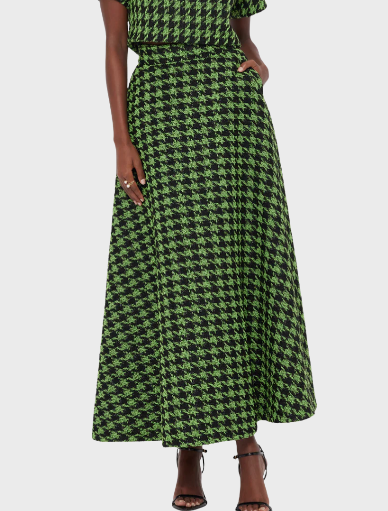 A model wears a green and black houndstooth patterned two-piece outfit, featuring a crop top and a long skirt, paired with strappy heels.