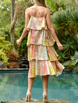 A woman in a striking multi-colored dress poses by a pool, reflecting the sunlight and creating a lively scene.